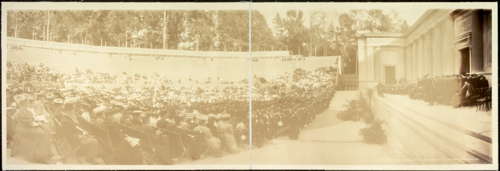 Panoramic photograph of a graduation ceremony in an open-air theatre at Berkeley in 1906: a seated crowd in hats faces a stage where gowned graduates stand before a columned wall.